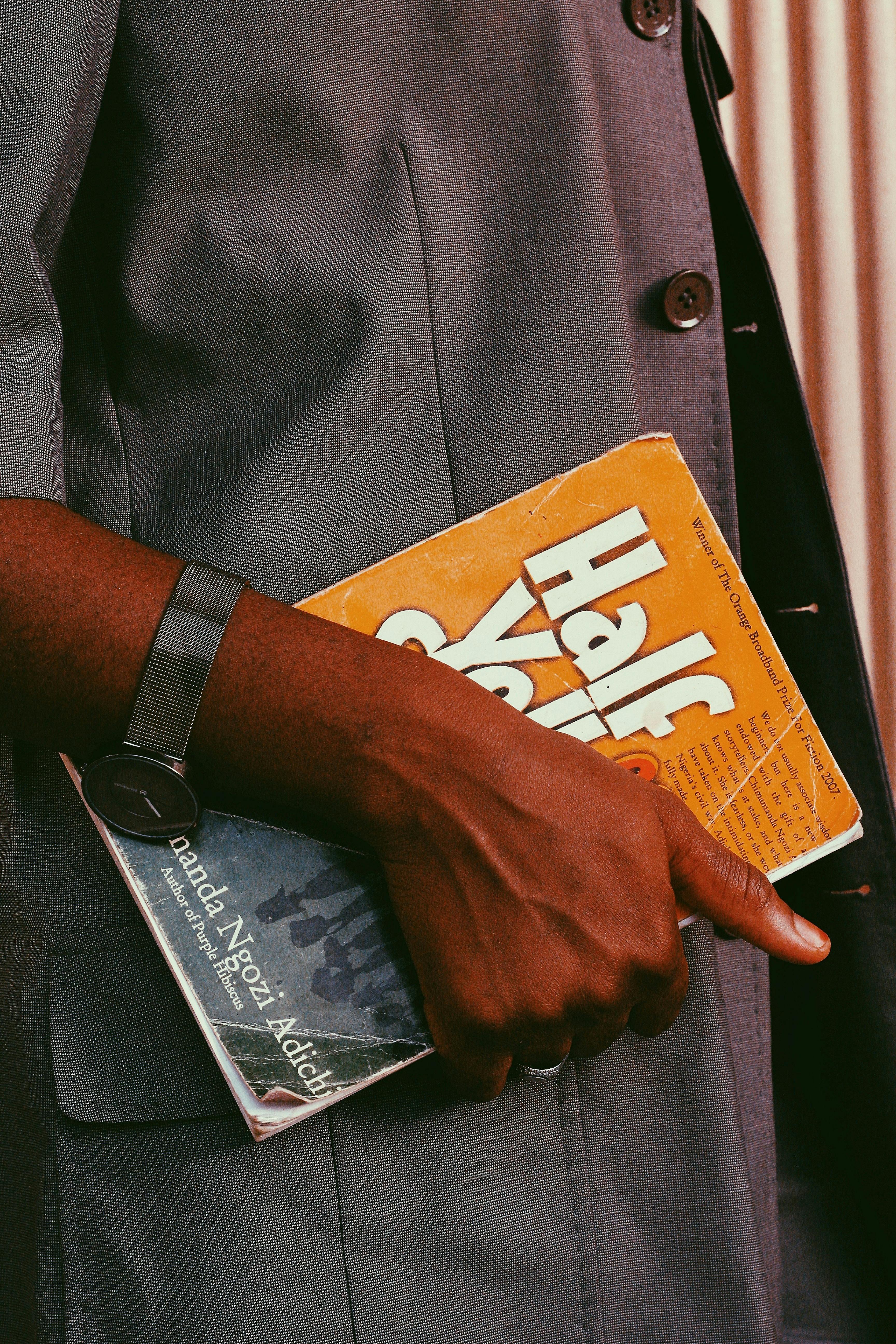 A person holds two books, including 'Half of a Yellow Sun,' in Abuja, Nigeria, showcasing literature and style.